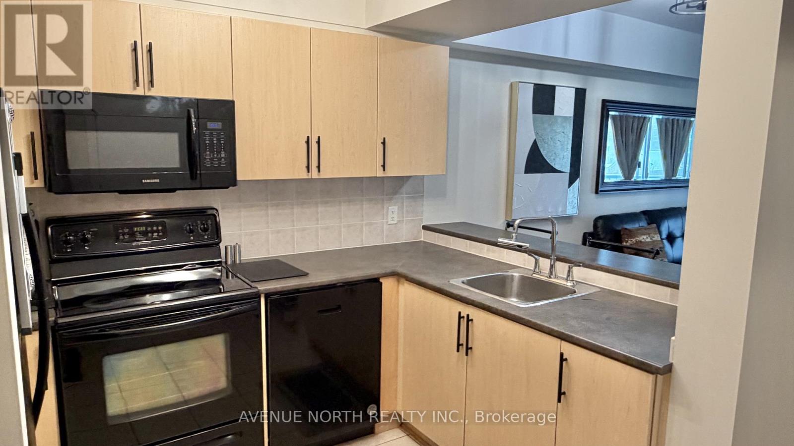 A kitchen with a black oven and microwave, a sink, and cabinets.