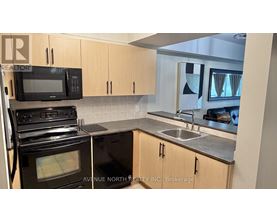 A kitchen with a black oven and microwave, a sink, and cabinets.
