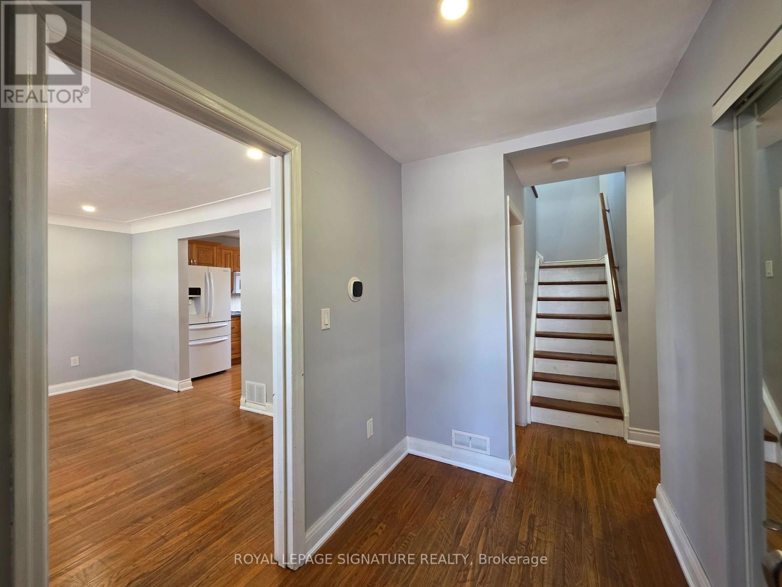 A room with wooden floors and white walls, with a staircase leading to another level.