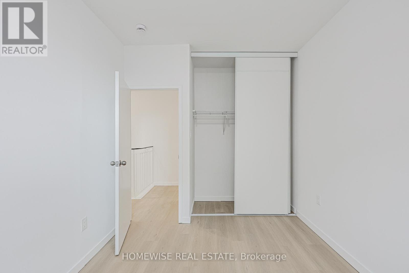 A white bedroom with a doorway leading to another room.
