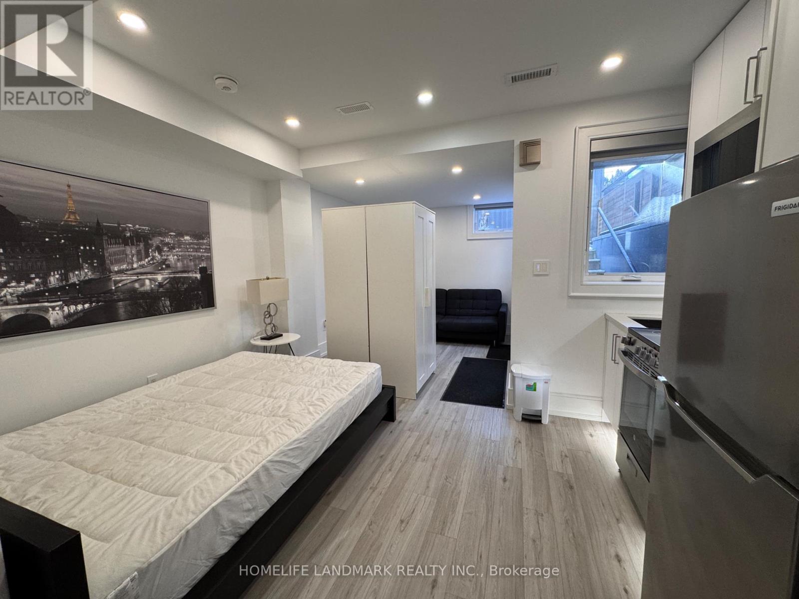 A bedroom with a large bed and a kitchen area in the background.