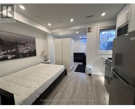 A bedroom with a large bed and a kitchen area in the background.