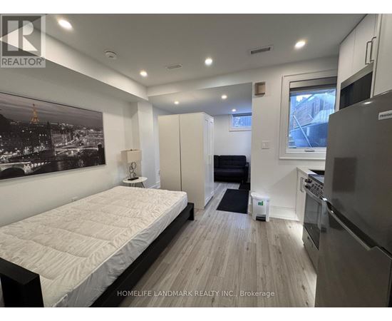 A bedroom with a large bed and a kitchen area in the background.