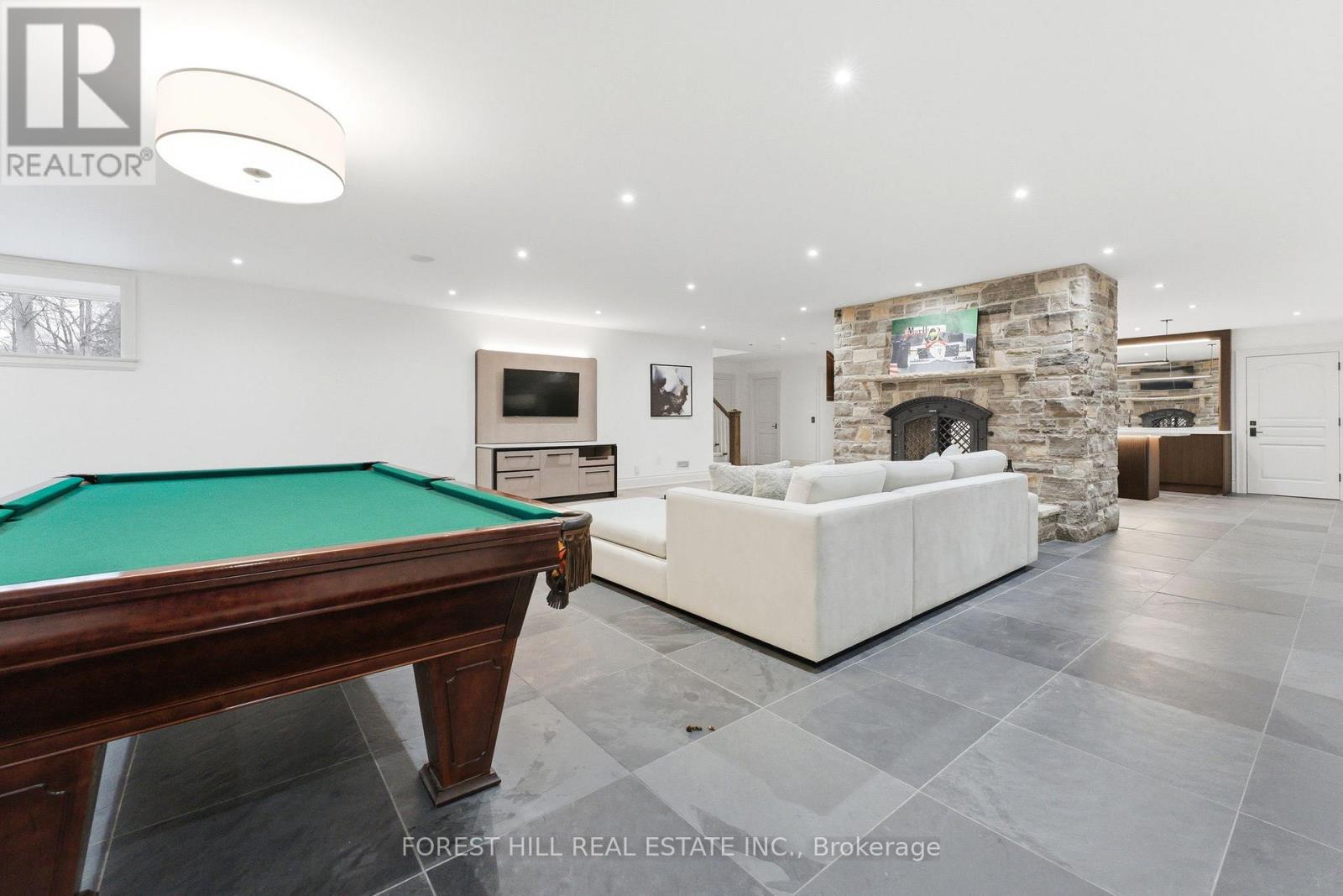 A pool table is in the middle of a spacious room with a stone fireplace.