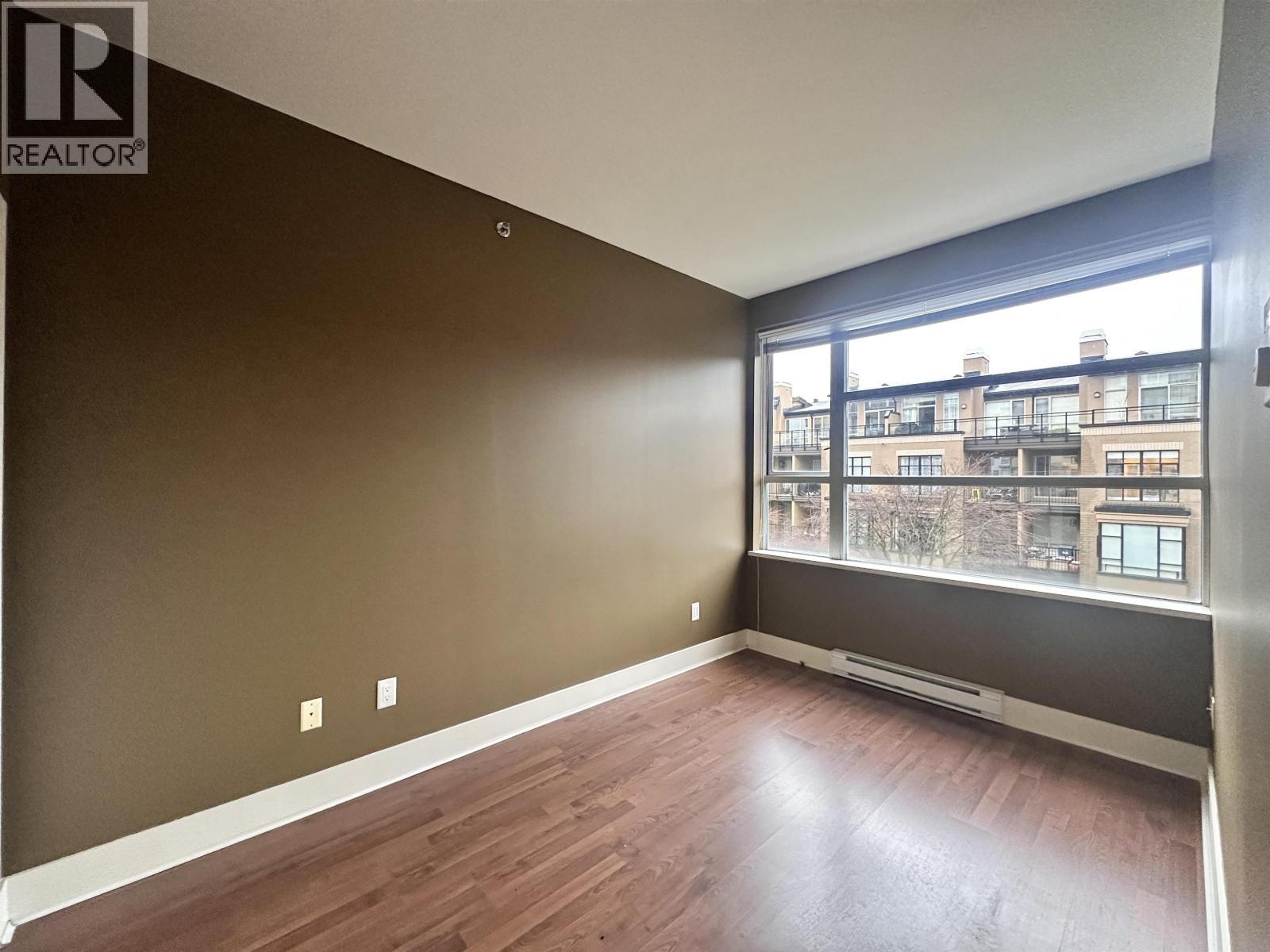 A room with brown walls and wooden flooring with a window overlooking a cityscape.