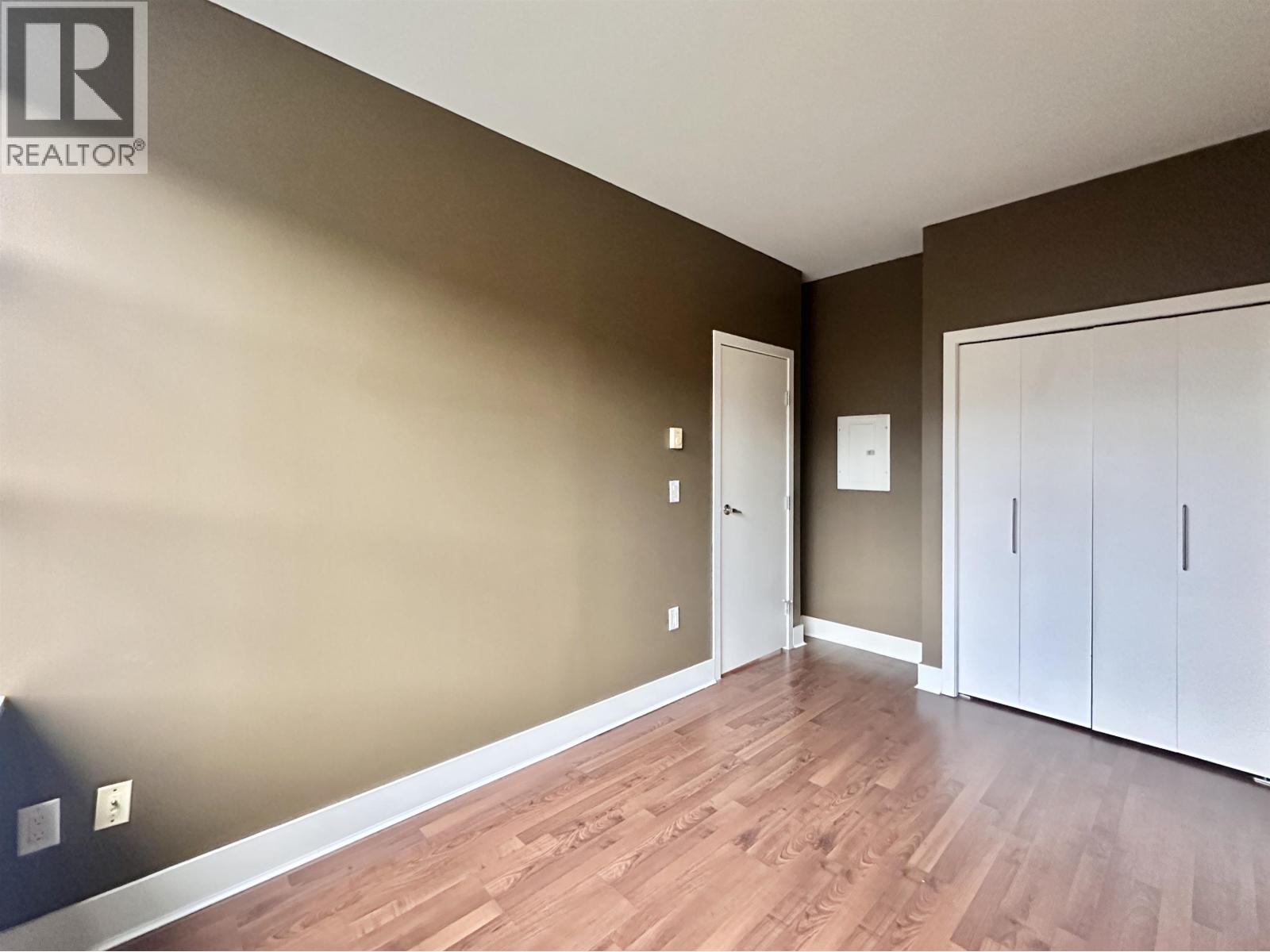 A room with brown walls and wooden flooring, with a white door and cabinetry.