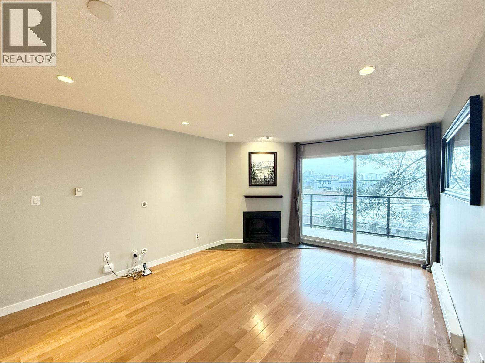 A spacious room with wooden flooring and a fireplace.