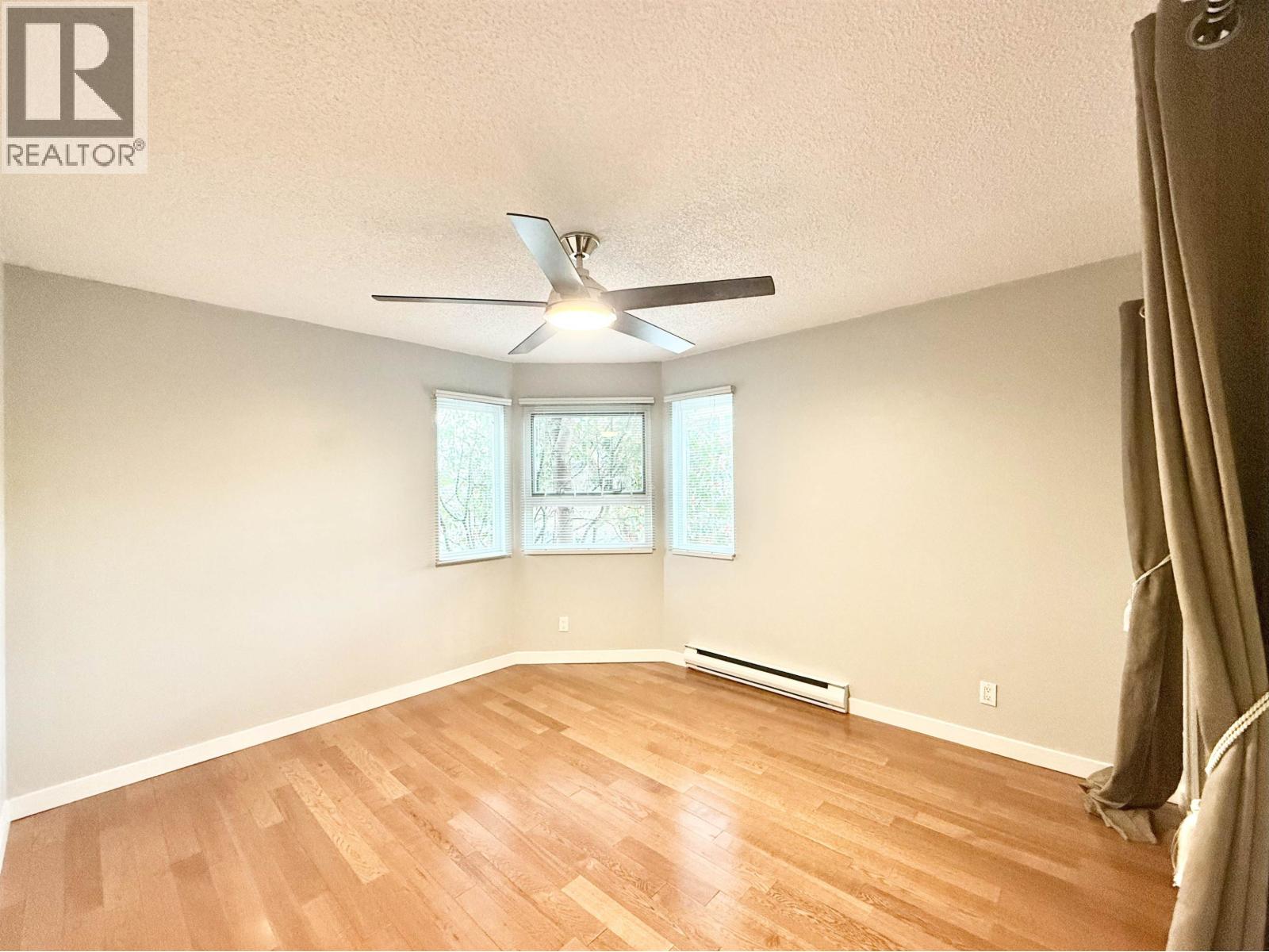 A room with a ceiling fan and a window with a view of trees.