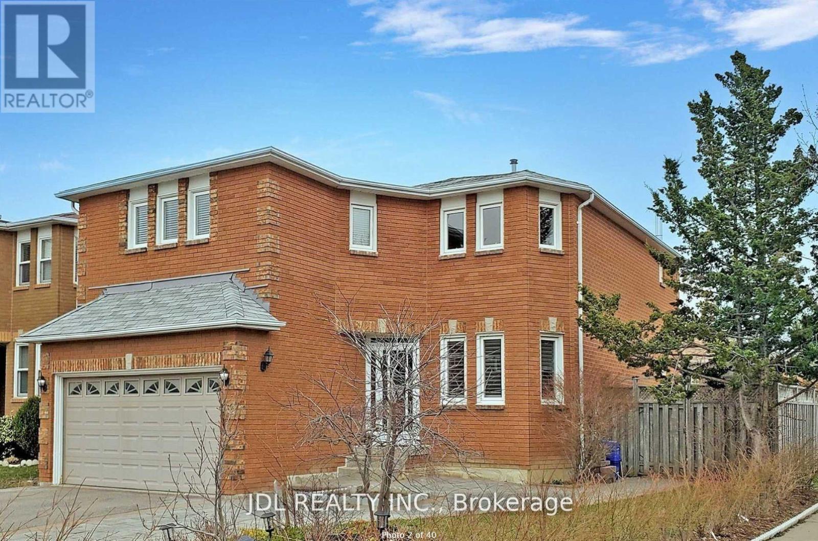 A red brick house with a garage door and a tree in front.