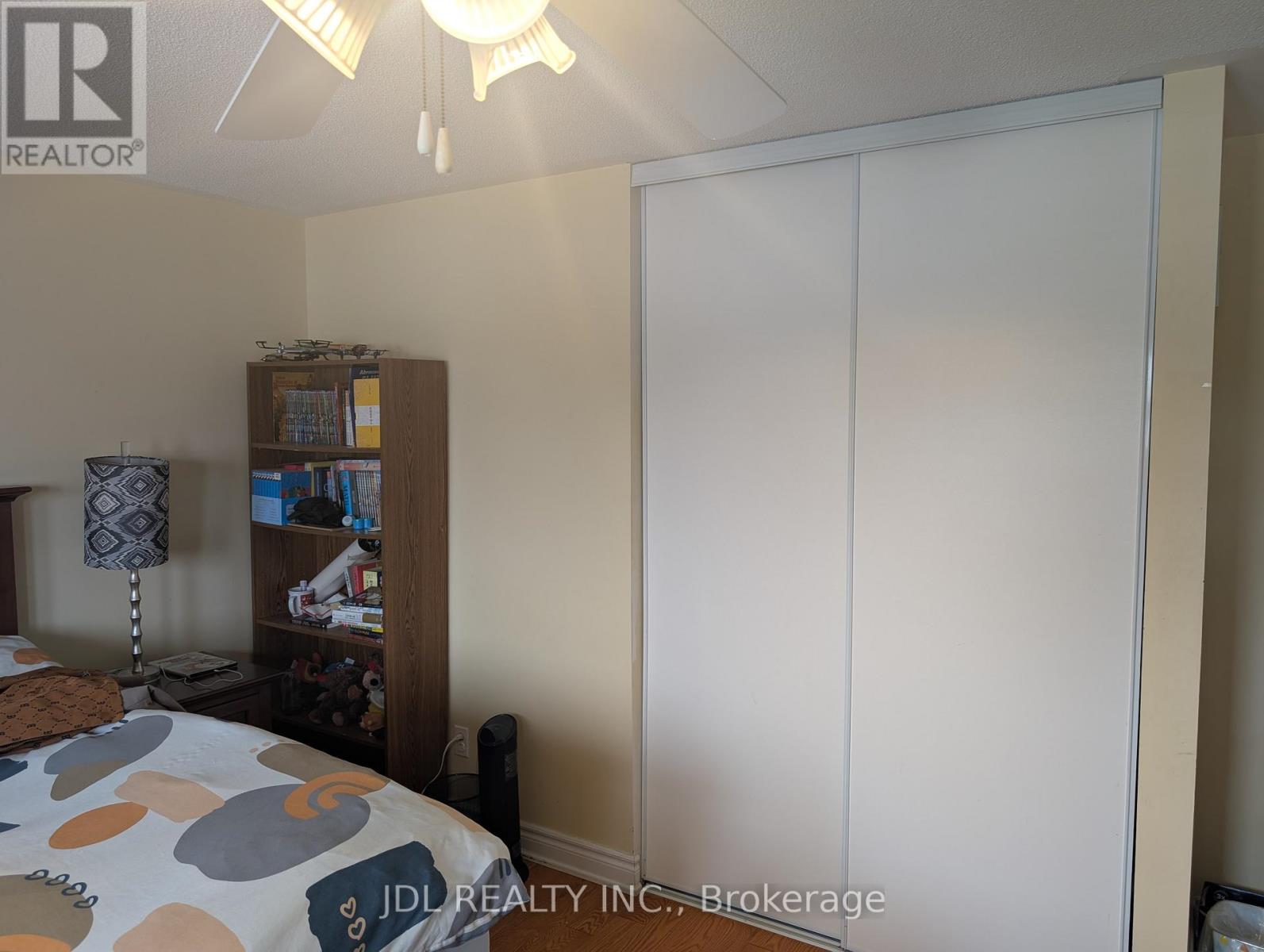 A bedroom with a bed, a nightstand with a lamp, a bookshelf, and a large white wardrobe.