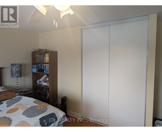 A bedroom with a bed, a nightstand with a lamp, a bookshelf, and a large white wardrobe.