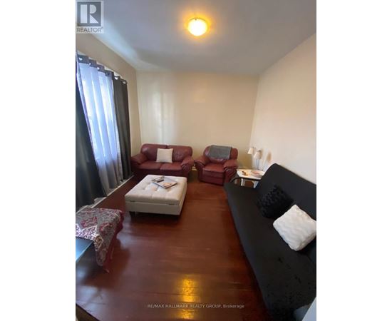 A living room with a red couch, a white ottoman, and a black couch with pillows.