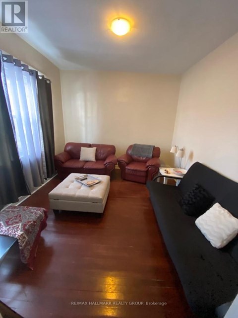 A living room with a red couch, a white ottoman, and a black couch with pillows.