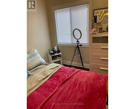 A bedroom with a red bedspread and a tripod in the corner.