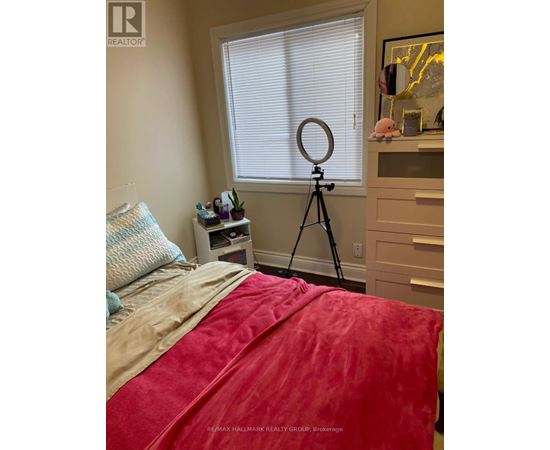 A bedroom with a red bedspread and a tripod in the corner.
