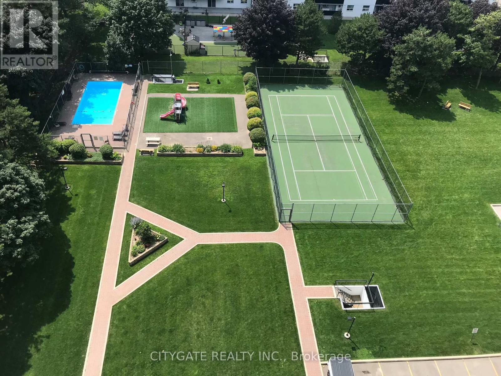 A tennis court is surrounded by a green lawn and a pool.