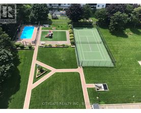A tennis court is surrounded by a green lawn and a pool.