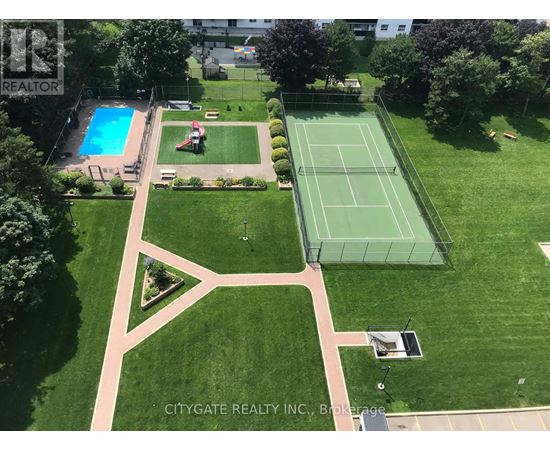 A tennis court is surrounded by a green lawn and a pool.