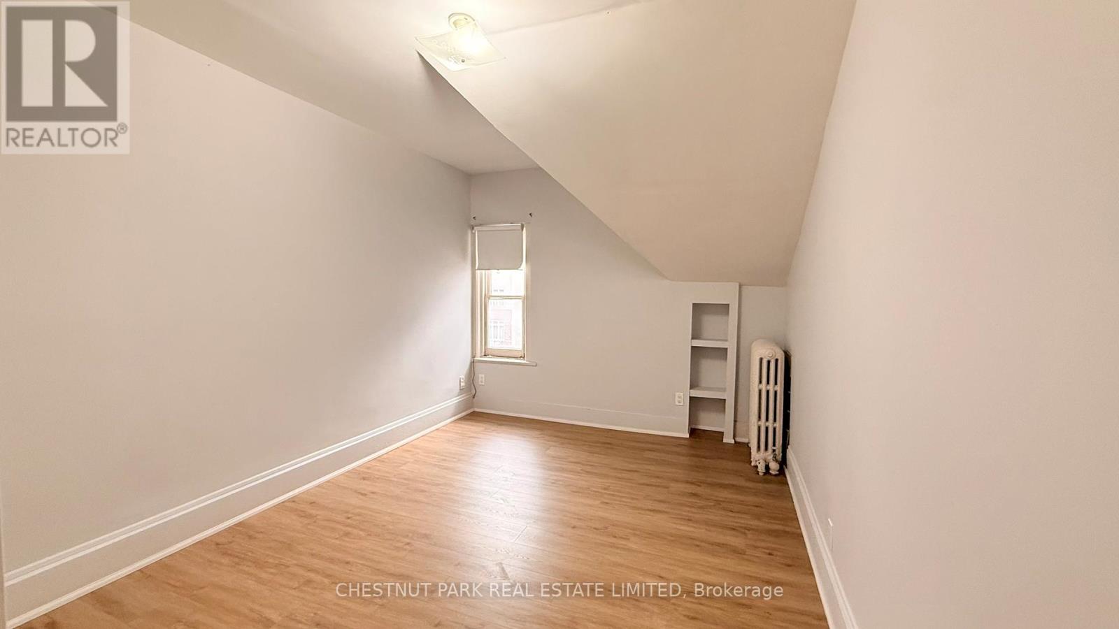A room with a wood floor and white walls, with a window and a radiator.