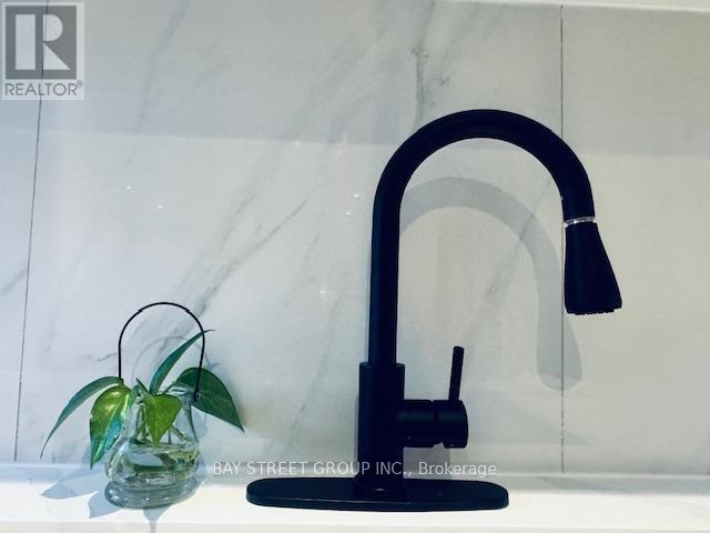 A modern kitchen sink with a black faucet and a green plant in a glass vase.