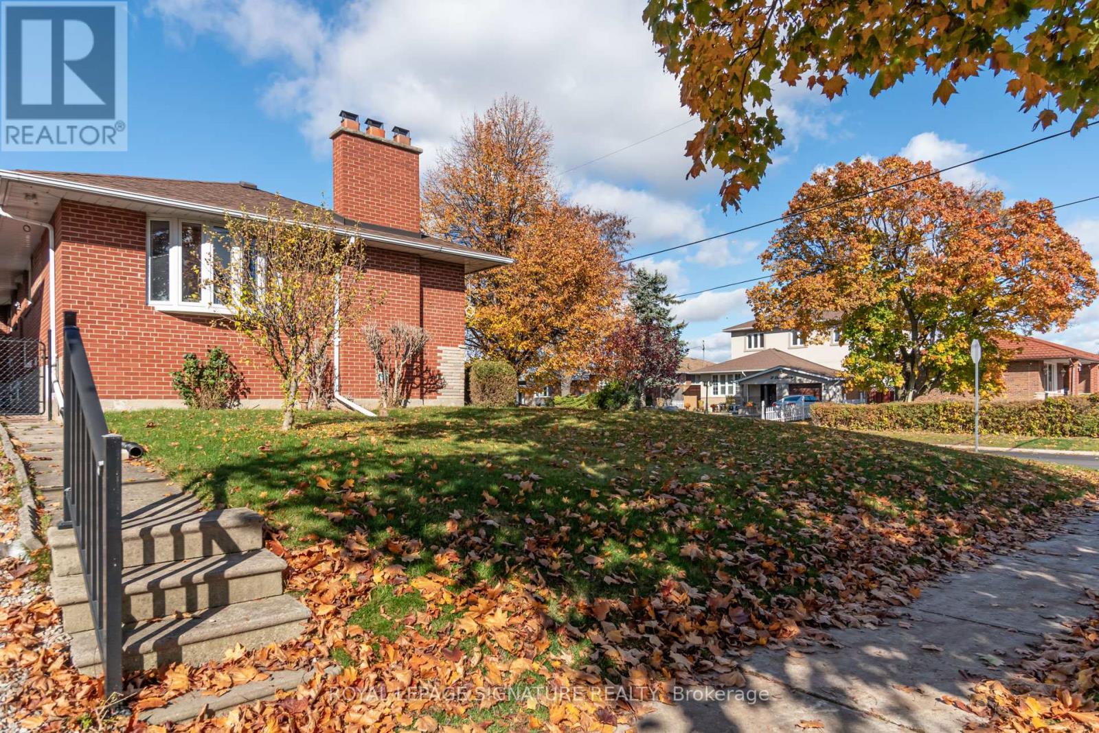 A house with a red brick exterior and a tree with orange leaves in front.