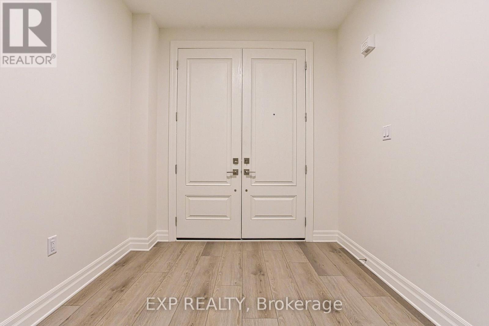 A white door with a black handle is in the middle of a room with wooden floors and white walls.