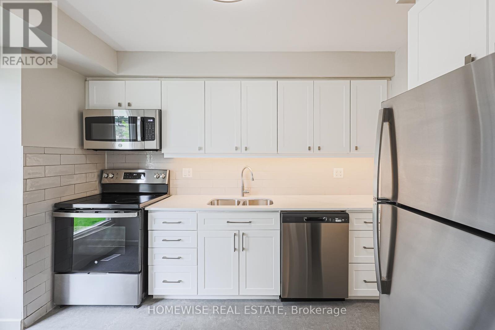 A kitchen with a refrigerator, oven, microwave, and sink.