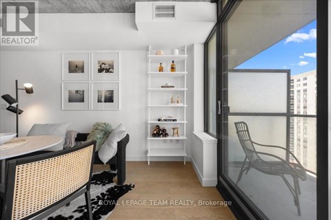 A modern living room with a glass table and chairs, a white sofa, and a shelf with bottles and decorations.