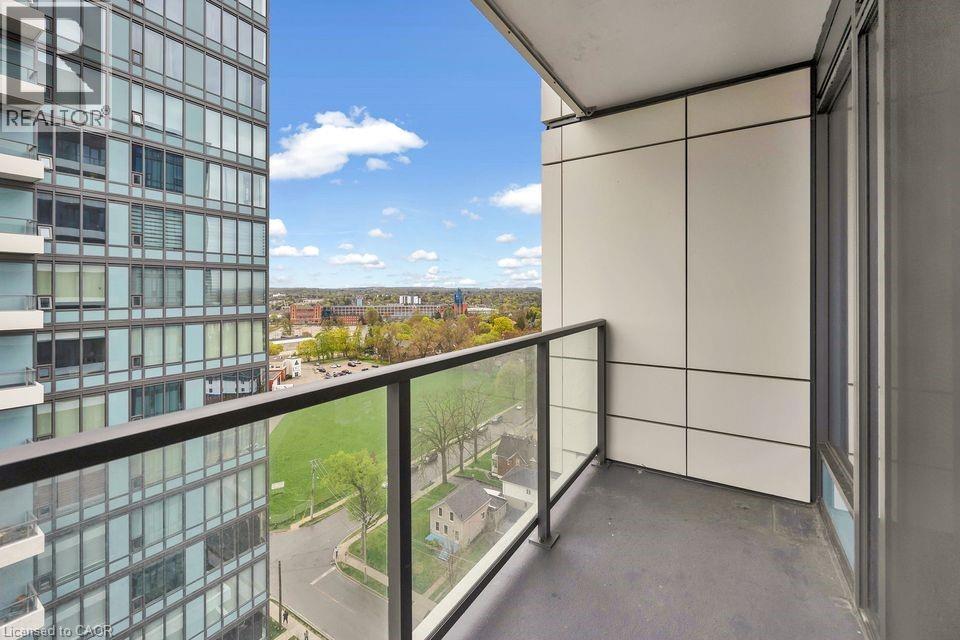 A balcony with a glass railing overlooks a parking lot and buildings.
