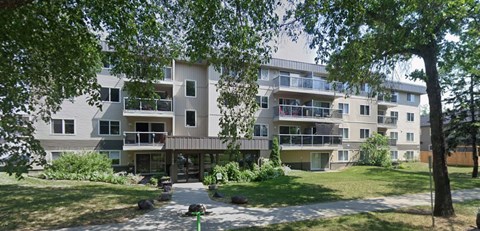 A large apartment building with balconies and a green lawn in front.