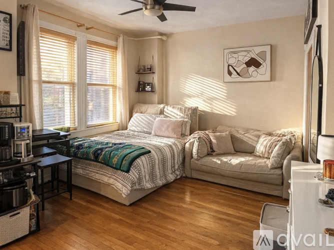 A bedroom with a bed and a couch, both covered with blankets, and a ceiling fan.