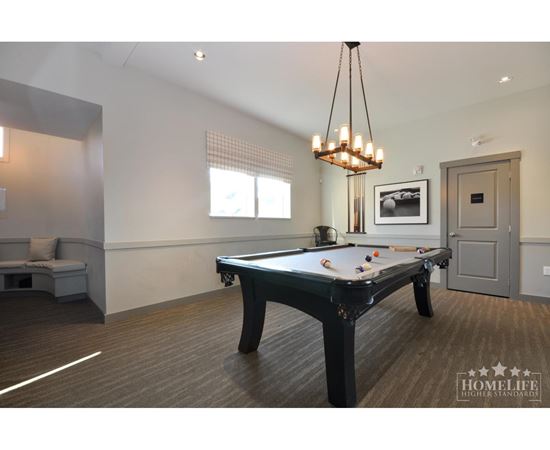 A pool table is in the middle of a room with a bench and a picture on the wall.
