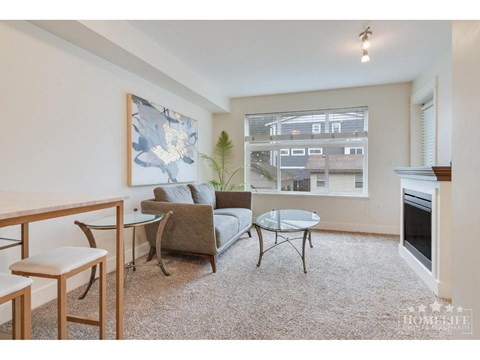 A living room with a grey couch, a glass table, and a painting on the wall.