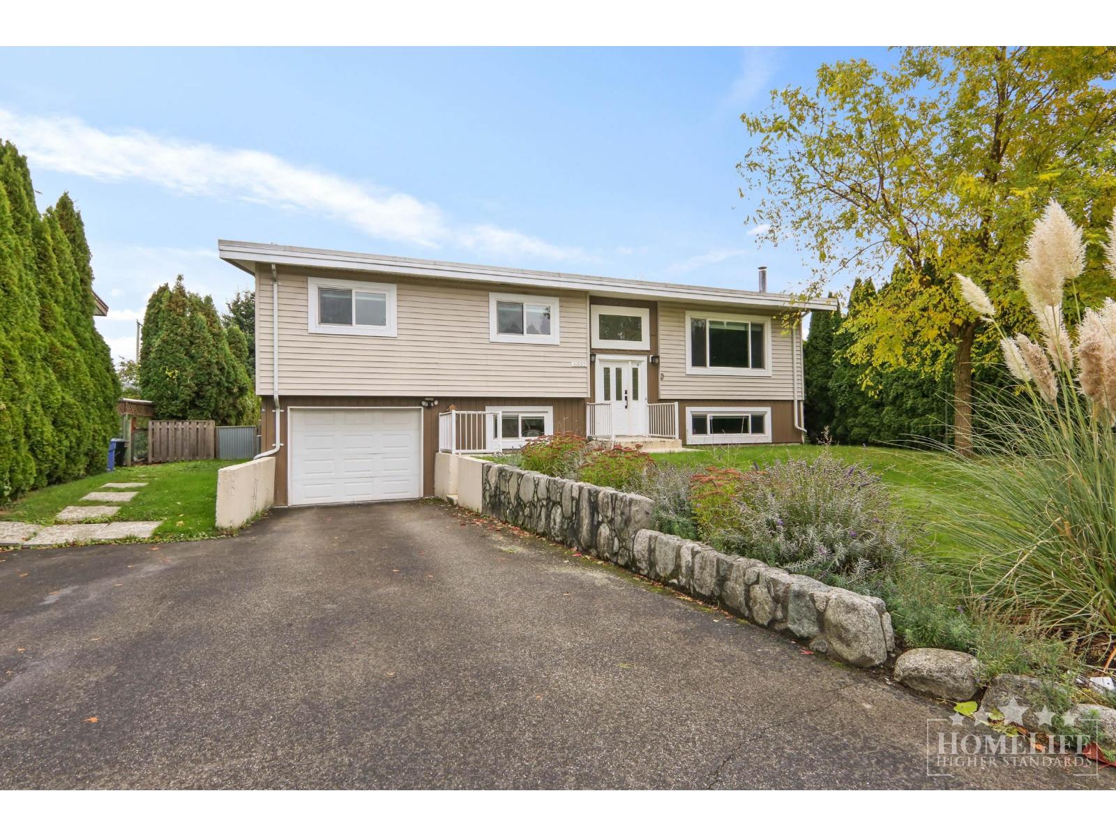 A two-story house with a garage is surrounded by a well-maintained lawn and a stone wall.