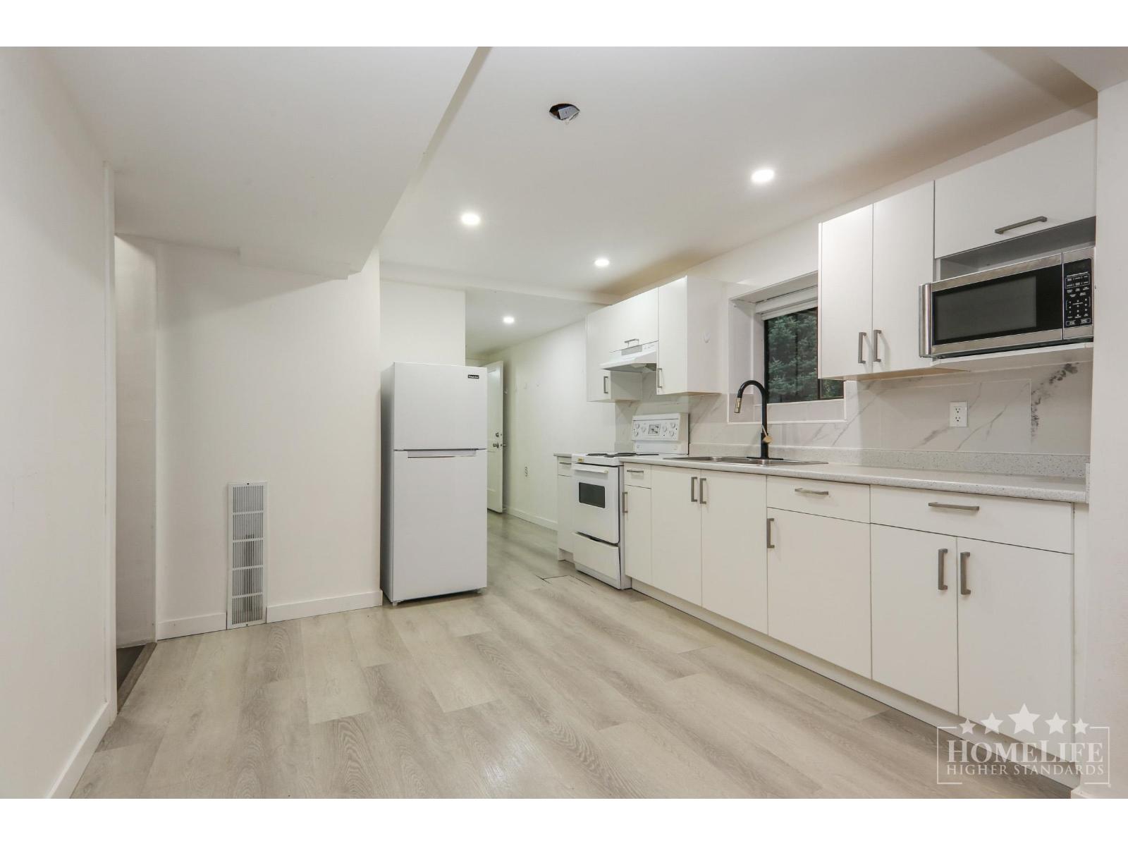 A kitchen with white cabinets and appliances in a white room.