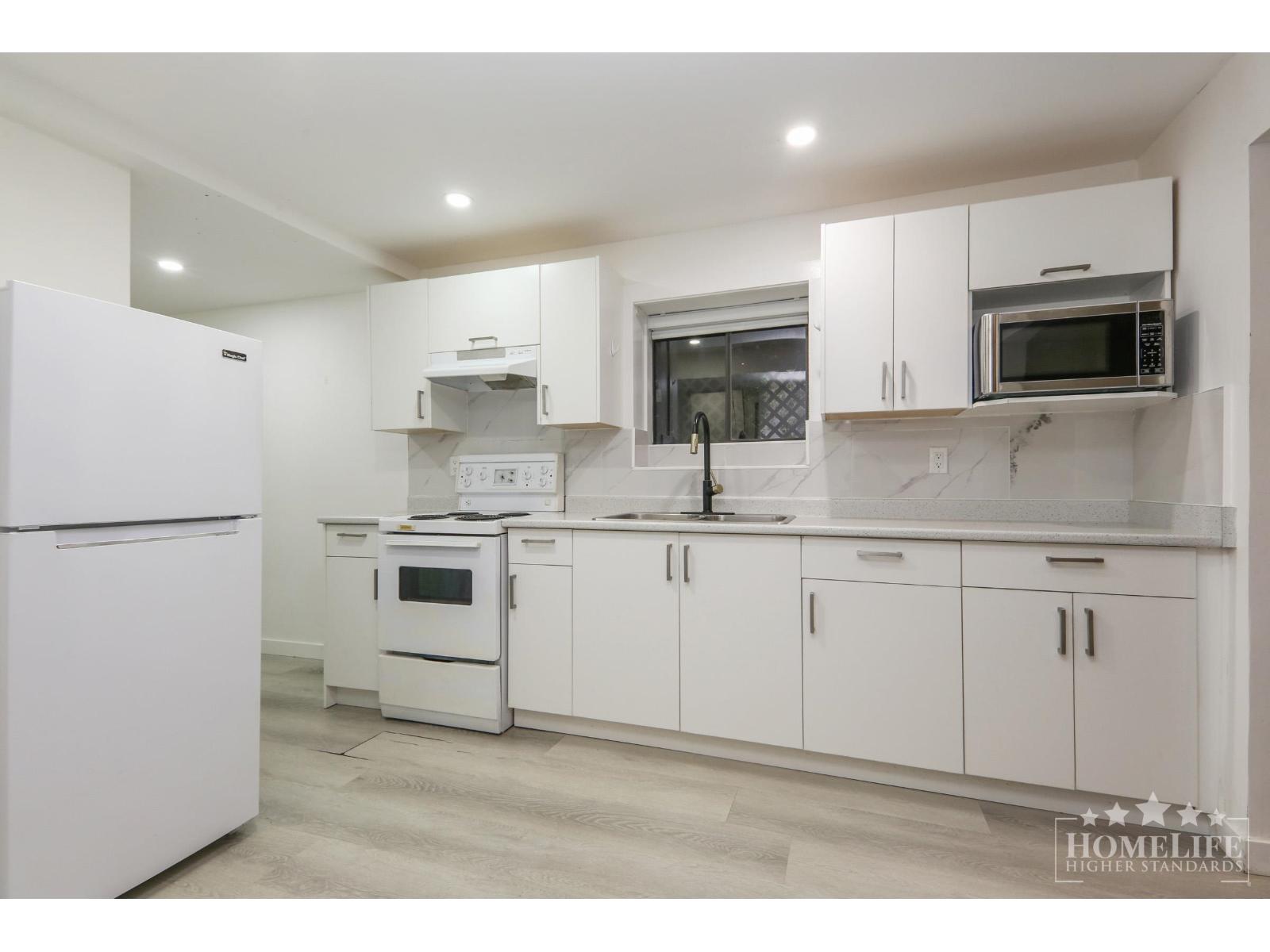 A white kitchen with a refrigerator on the left and a microwave on the right.