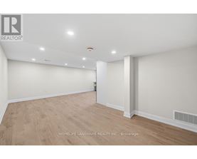A spacious room with wooden flooring and white walls, with a logo in the top left corner.