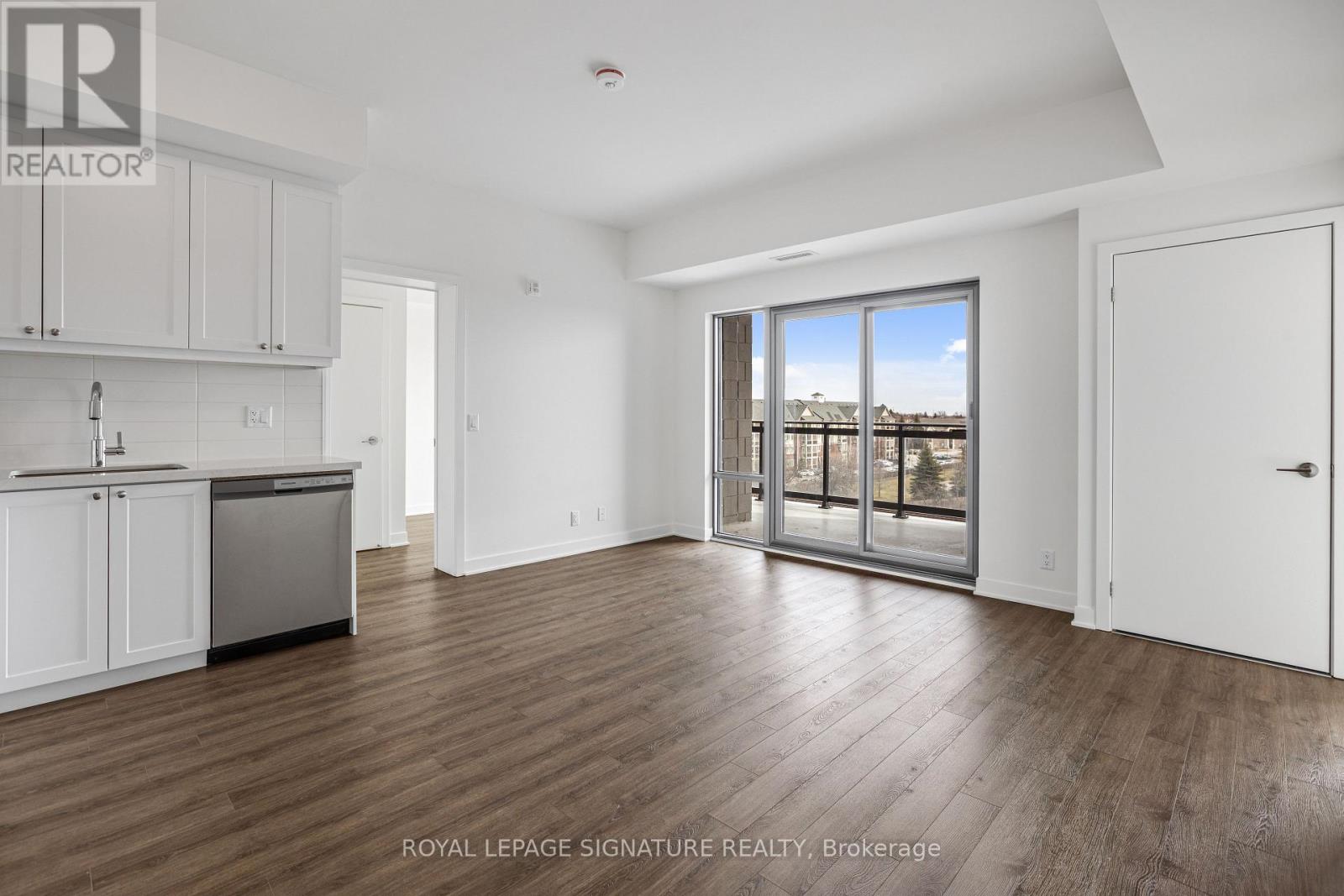 A spacious room with wooden flooring and a large window overlooking a body of water.