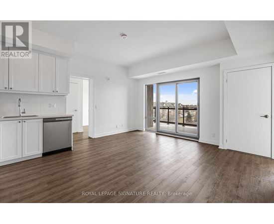 A spacious room with wooden flooring and a large window overlooking a body of water.