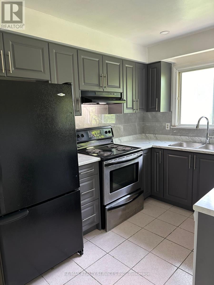 A black refrigerator is in a kitchen with grey cabinets.