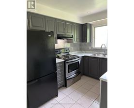 A black refrigerator is in a kitchen with grey cabinets.