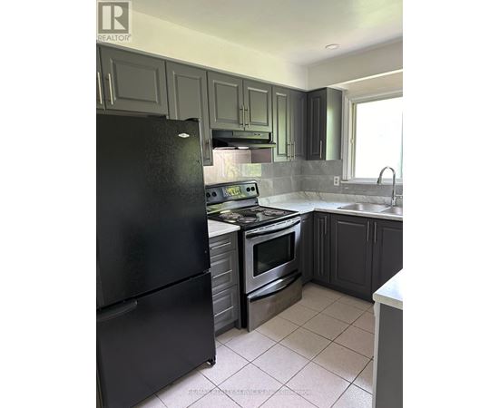 A black refrigerator is in a kitchen with grey cabinets.