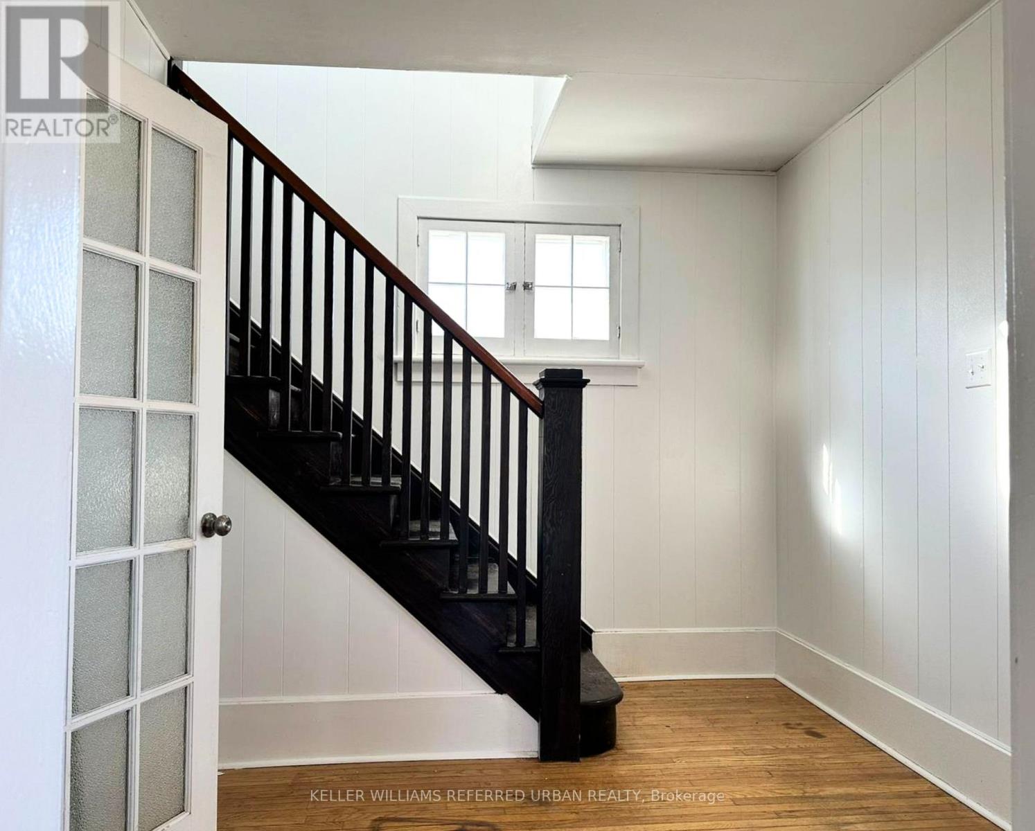 A white room with a wooden floor and a staircase with a black railing.