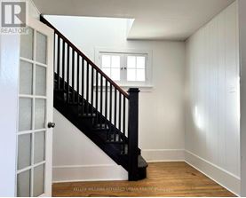 A white room with a wooden floor and a staircase with a black railing.