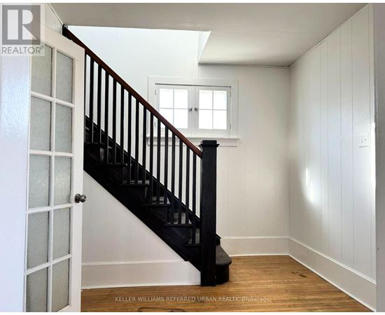 A white room with a wooden floor and a staircase with a black railing.