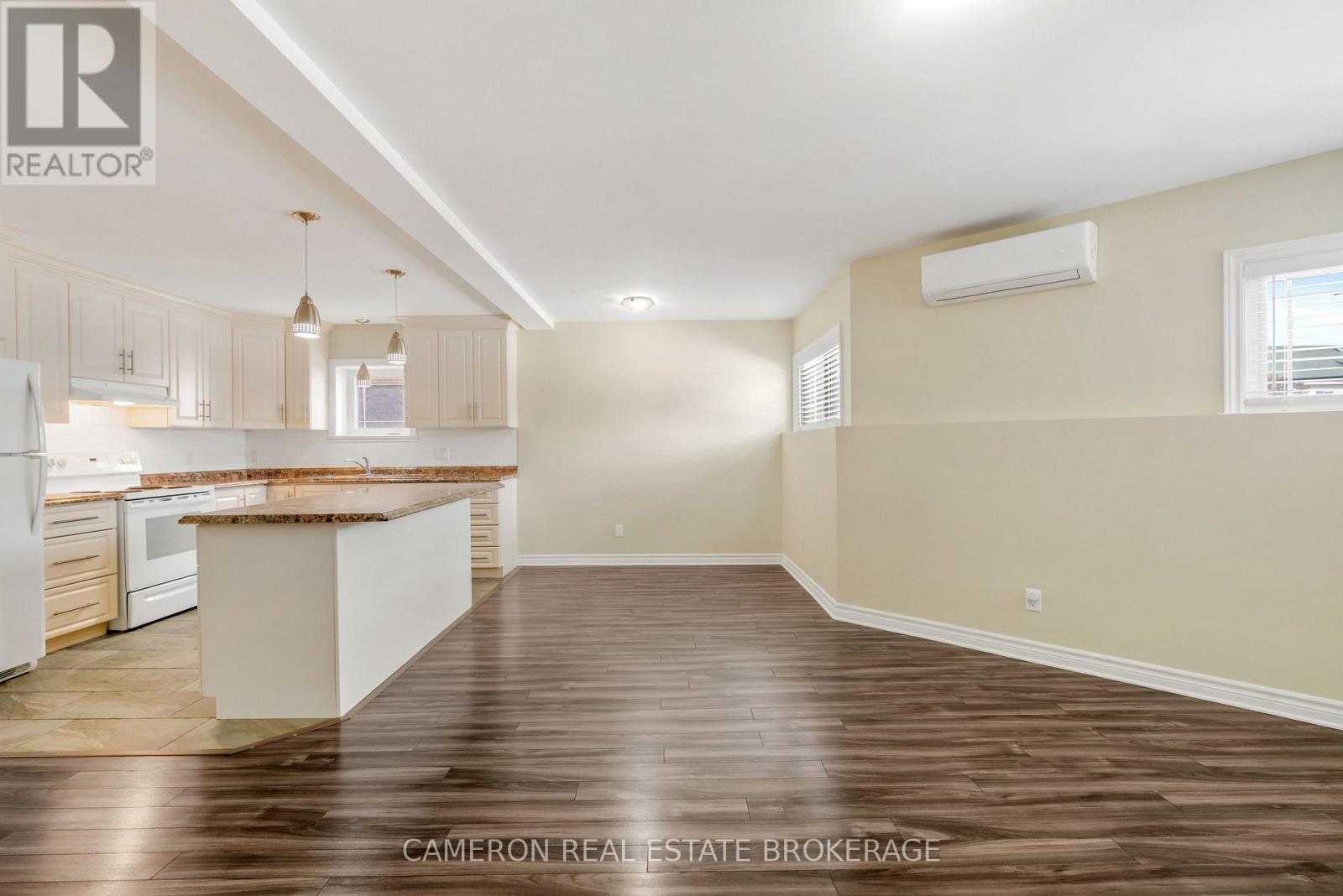 A well-lit, empty kitchen and living room with wooden floors and beige walls.