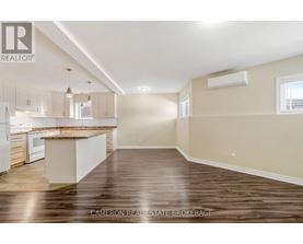 A well-lit, empty kitchen and living room with wooden floors and beige walls.
