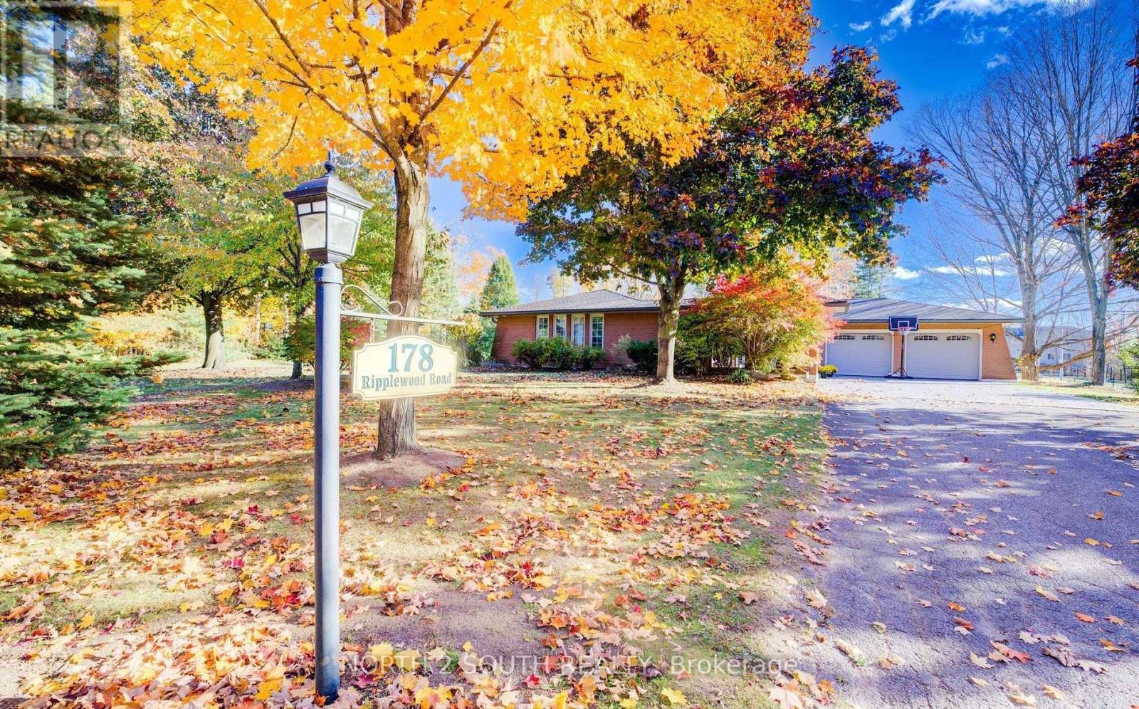 A street sign in front of a house with a tree full of yellow leaves.