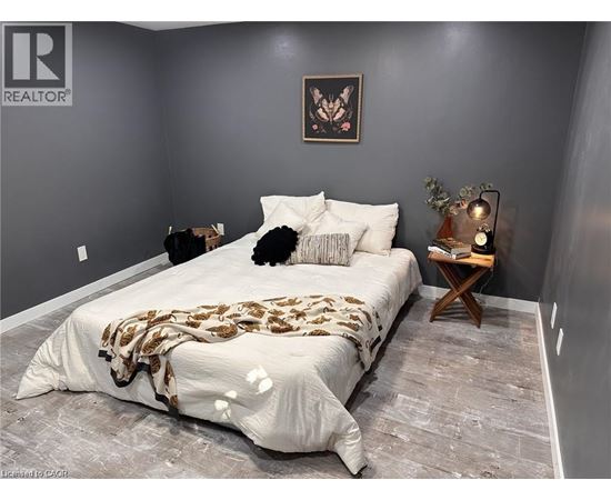 A bedroom with a bed covered in a patterned blanket and a small wooden table with a plant on it.