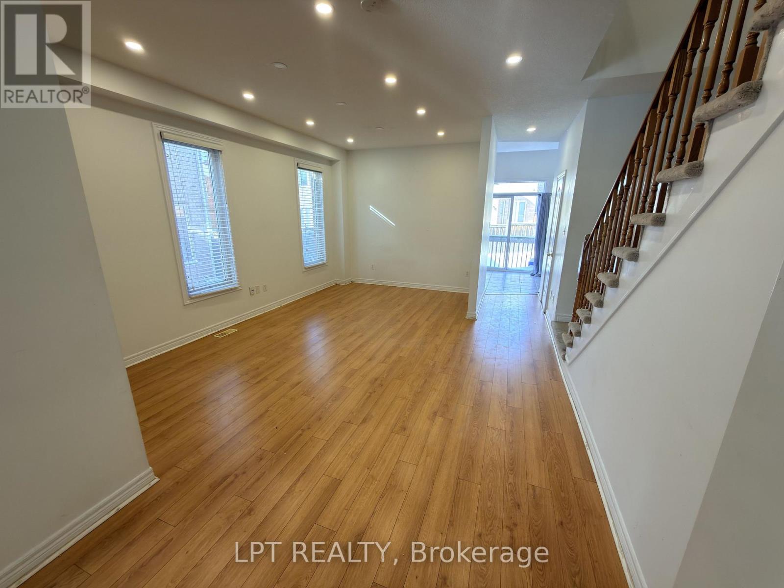 A spacious room with wooden floors and a staircase on the right side.